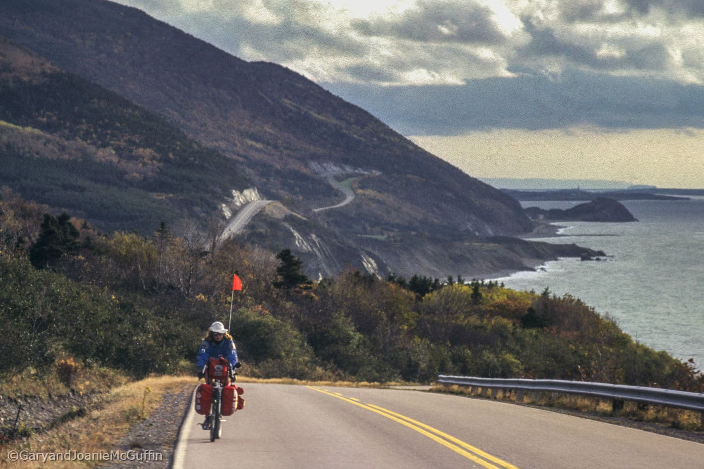 Biker on a highway with mountains and shore line in background